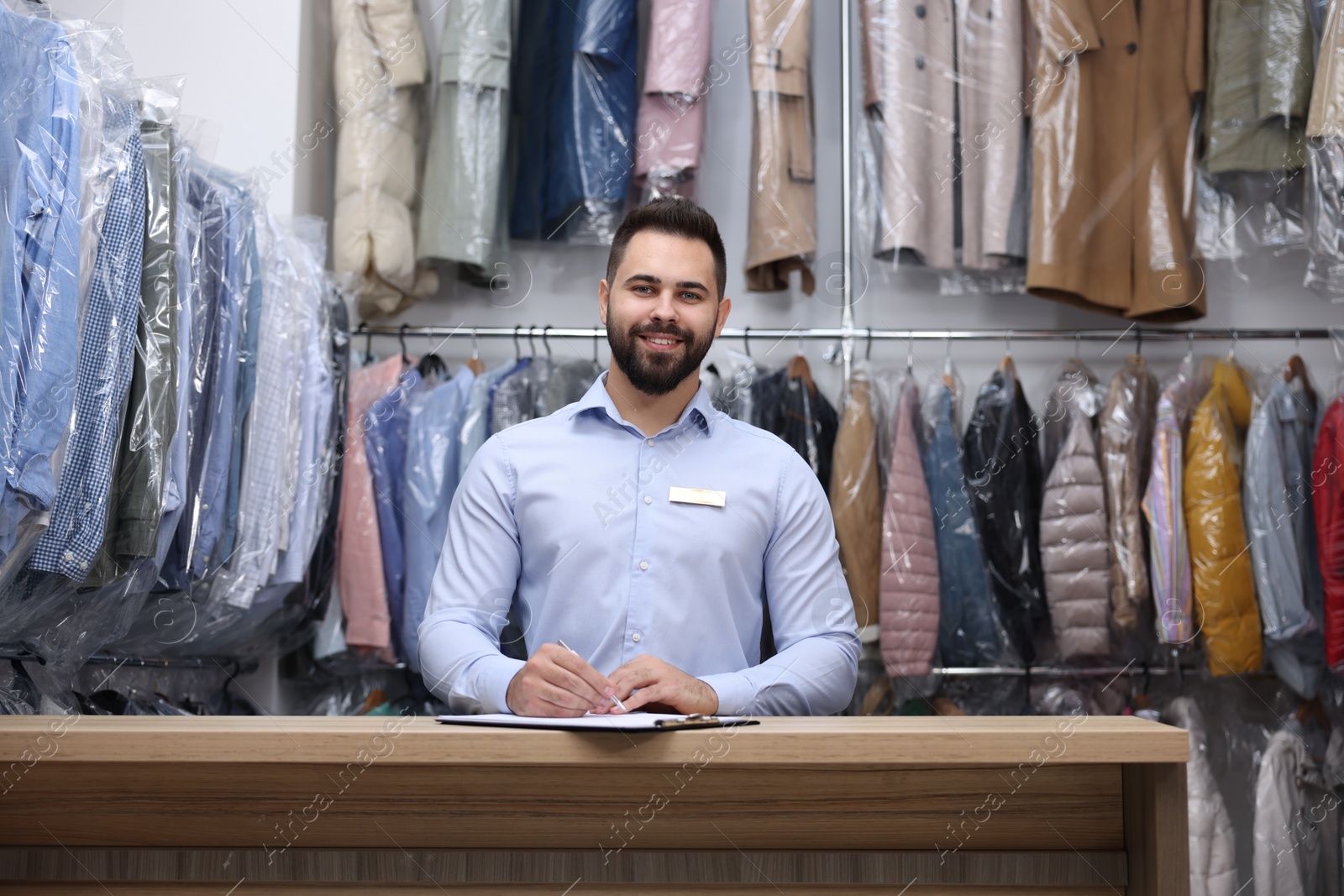 Photo of Dry-cleaning service. Happy worker at counter indoors