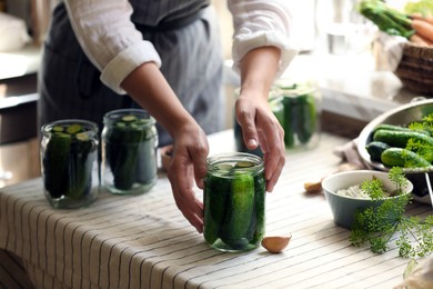 Photo of Woman canning delicious cucumbers in kitchen, closeup