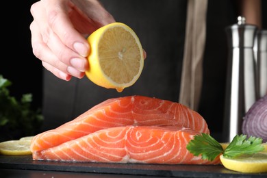 Photo of Woman squeezing lemon onto fresh raw salmon at table, closeup. Fish delicacy