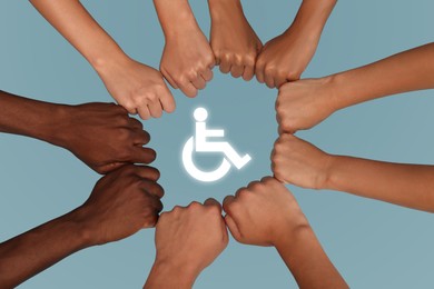 Inclusion concept. People holding fists together around international symbol of access together on light blue background, top view