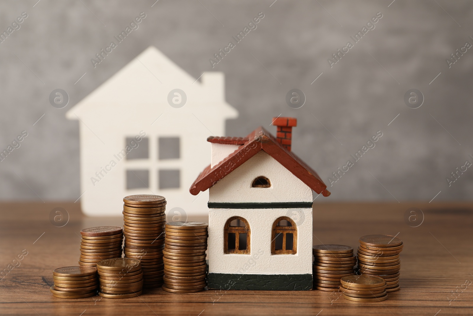 Photo of House models and stacked coins on wooden table against gray background