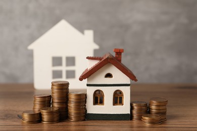 Photo of House models and stacked coins on wooden table against gray background