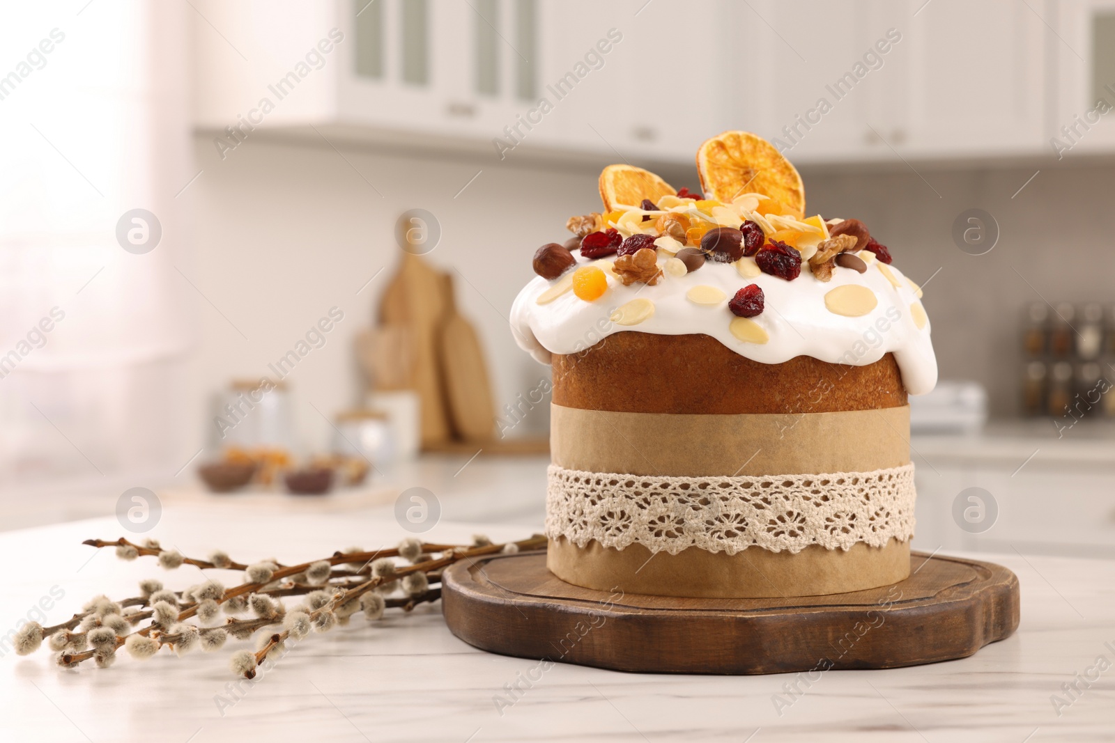 Photo of Delicious Easter cake with dried fruits and willow branches on white marble table in kitchen. Space for text