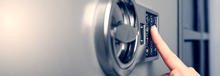 Woman opening steel safe with electronic lock, closeup. Banner design