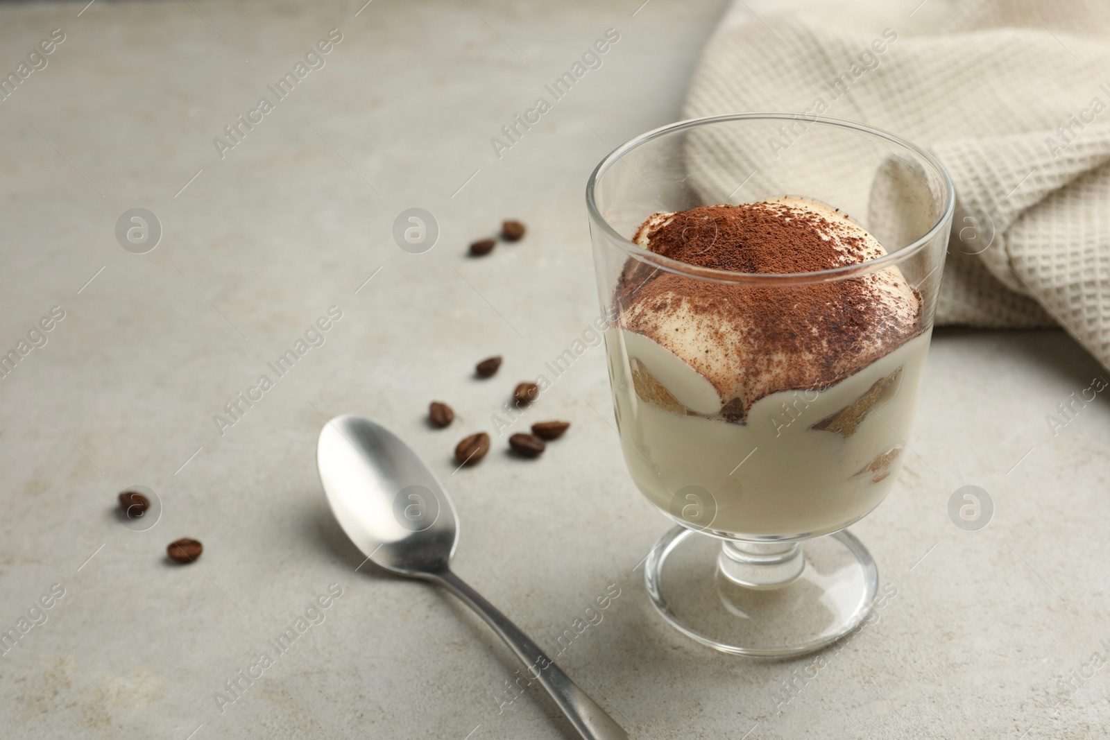 Photo of Delicious tiramisu in glass, spoon and scattered coffee beans on light table