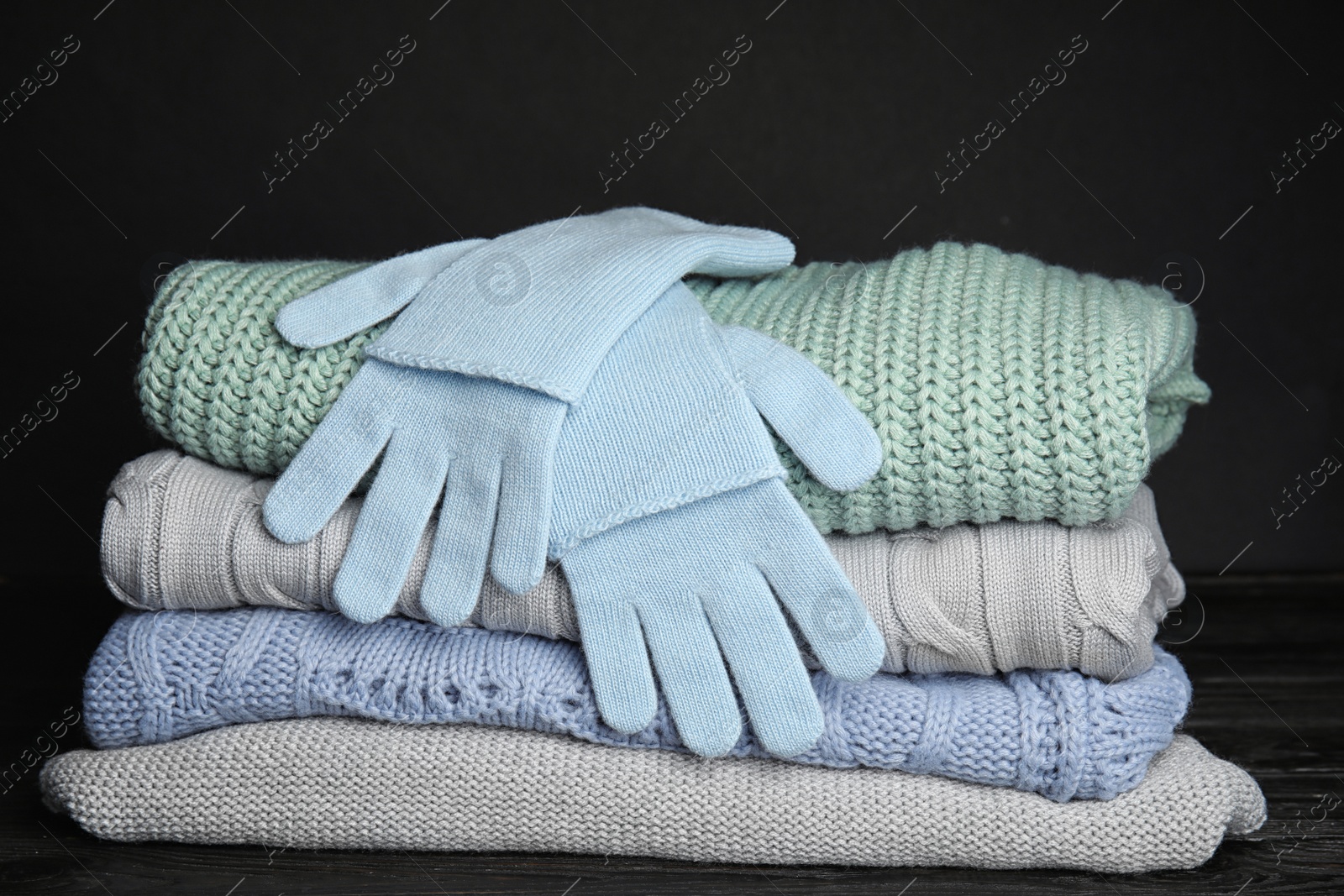 Photo of Stacked sweaters and gloves on table, closeup. Autumn clothes