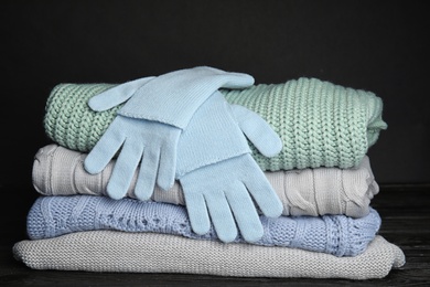 Photo of Stacked sweaters and gloves on table, closeup. Autumn clothes