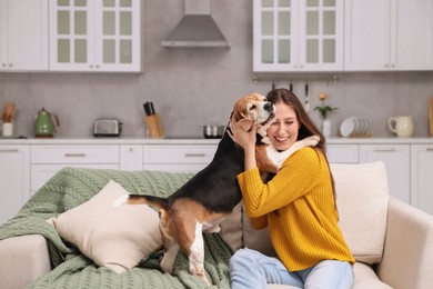 Happy young woman with her cute Beagle dog on couch at home. Lovely pet