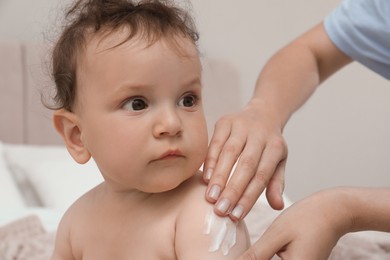 Photo of Mother applying body cream on her baby indoors, closeup