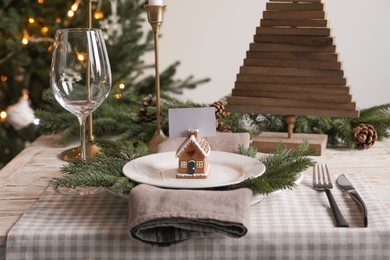 Festive place setting with beautiful dishware, cutlery and gingerbread house card holder for Christmas dinner on wooden table