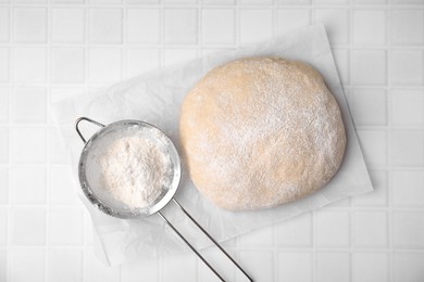 Photo of Fresh dough and sieve with flour on white tiled table, top view