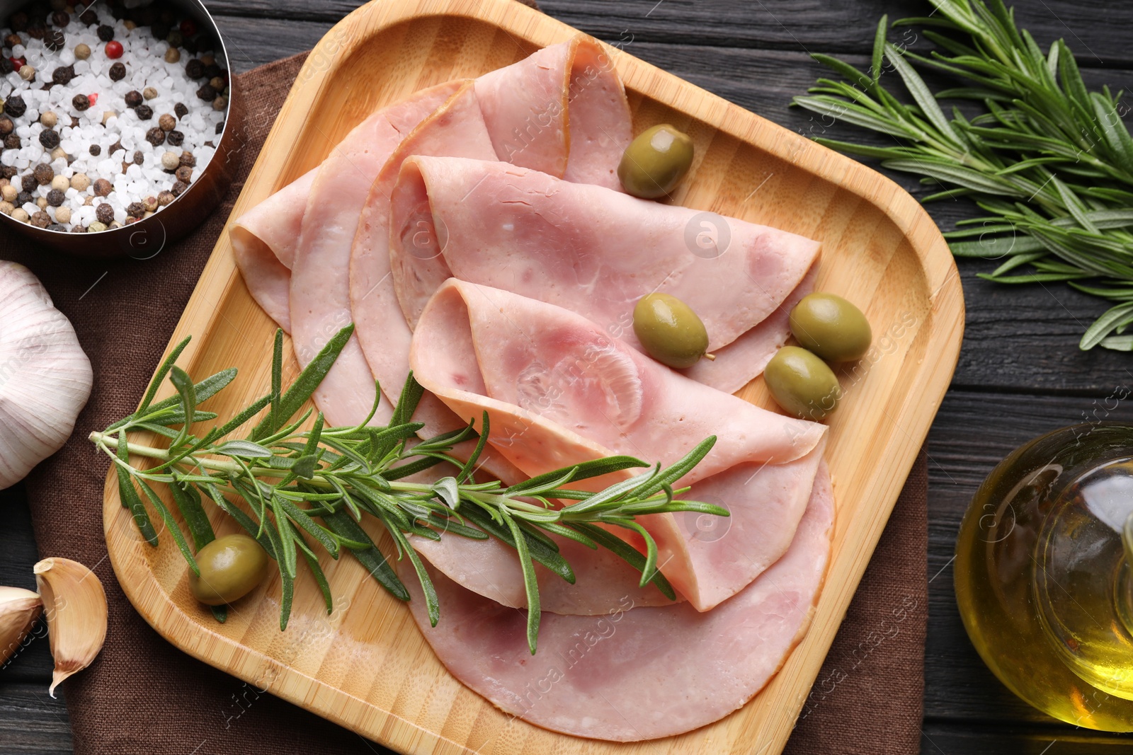 Photo of Slices of delicious ham with rosemary and olives served on dark wooden table, flat lay