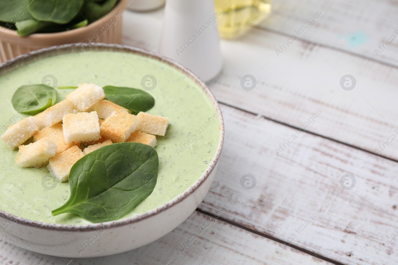 Photo of Delicious spinach cream soup with leaves and croutons in bowl on white wooden table, closeup. Space for text