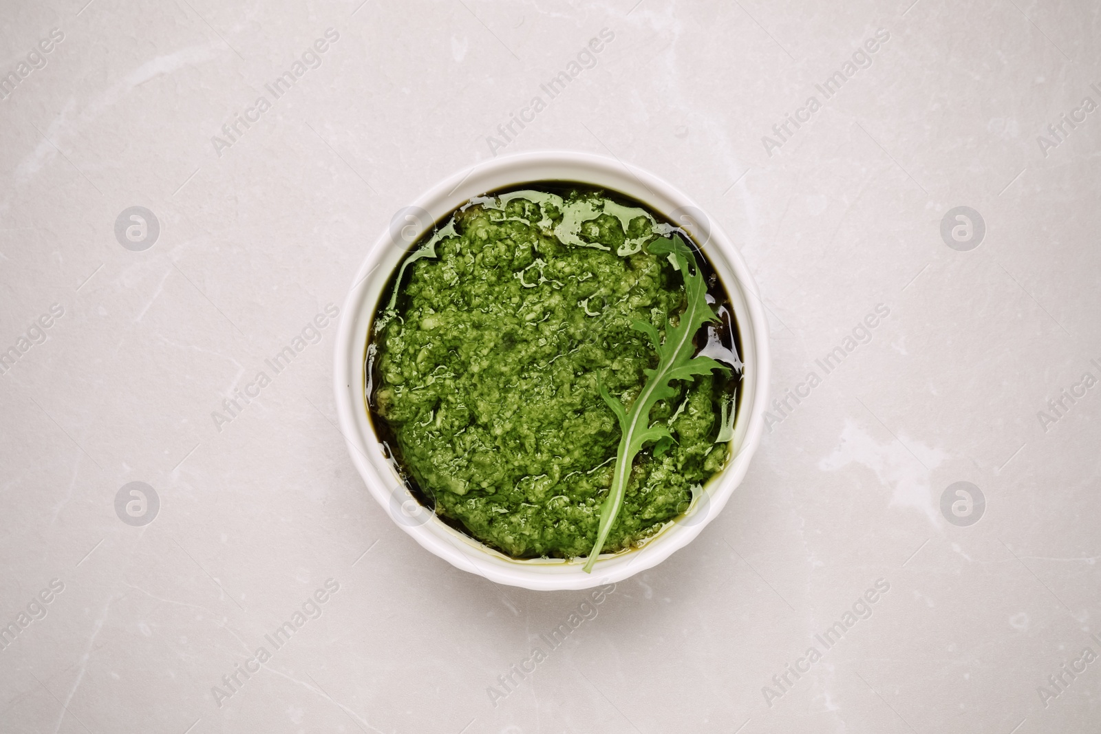 Photo of Bowl of tasty arugula pesto on light table, top view