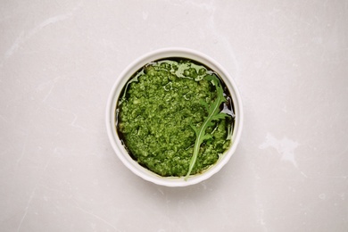 Bowl of tasty arugula pesto on light table, top view