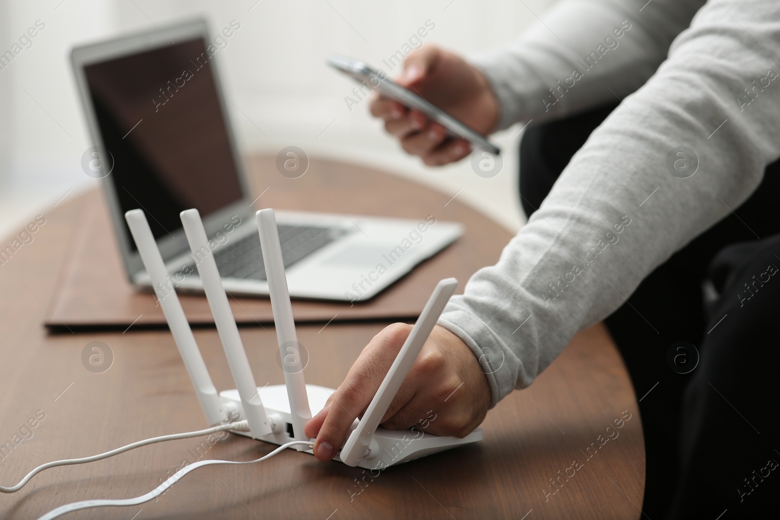 Photo of Man with smartphone and laptop connecting to internet via Wi-Fi router at wooden table, closeup