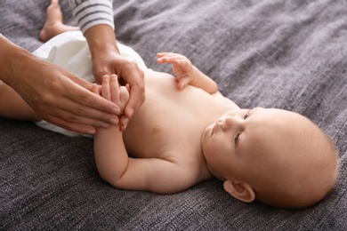 Young woman massaging cute little baby on blanket