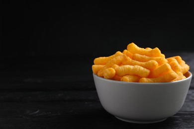 Photo of Bowl with crunchy cheesy corn snack on black wooden table. Space for text
