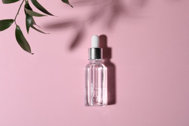 Bottle of cosmetic oil and green leaves on pink background, top view