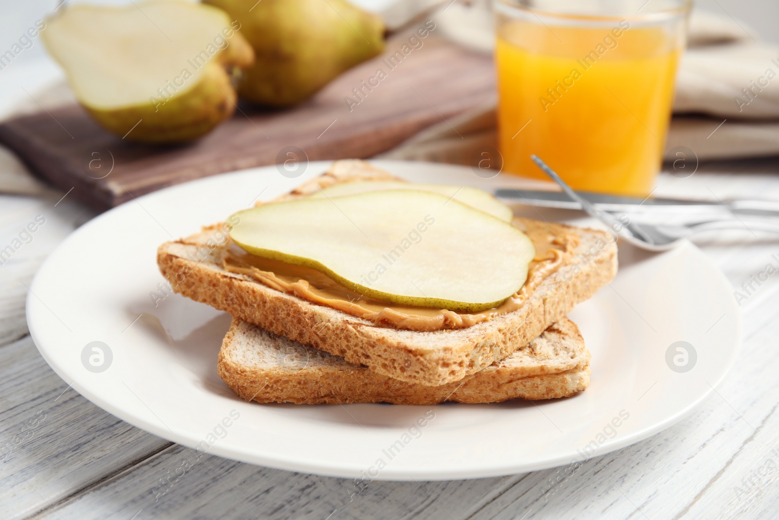 Photo of Slice of bread with peanut butter and pear on white wooden table