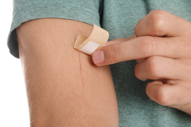 Photo of Man putting sticking plaster onto arm against on background, closeup