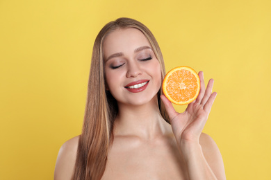 Photo of Young woman with cut orange on yellow background. Vitamin rich food