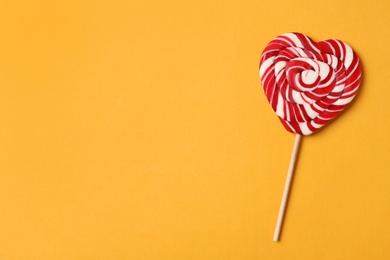 Sweet heart shaped lollipop on orange background, top view with space for text. Valentine's day celebration