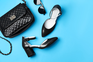 Stylish black female shoes, bag and glasses on light blue background, flat lay. Space for text