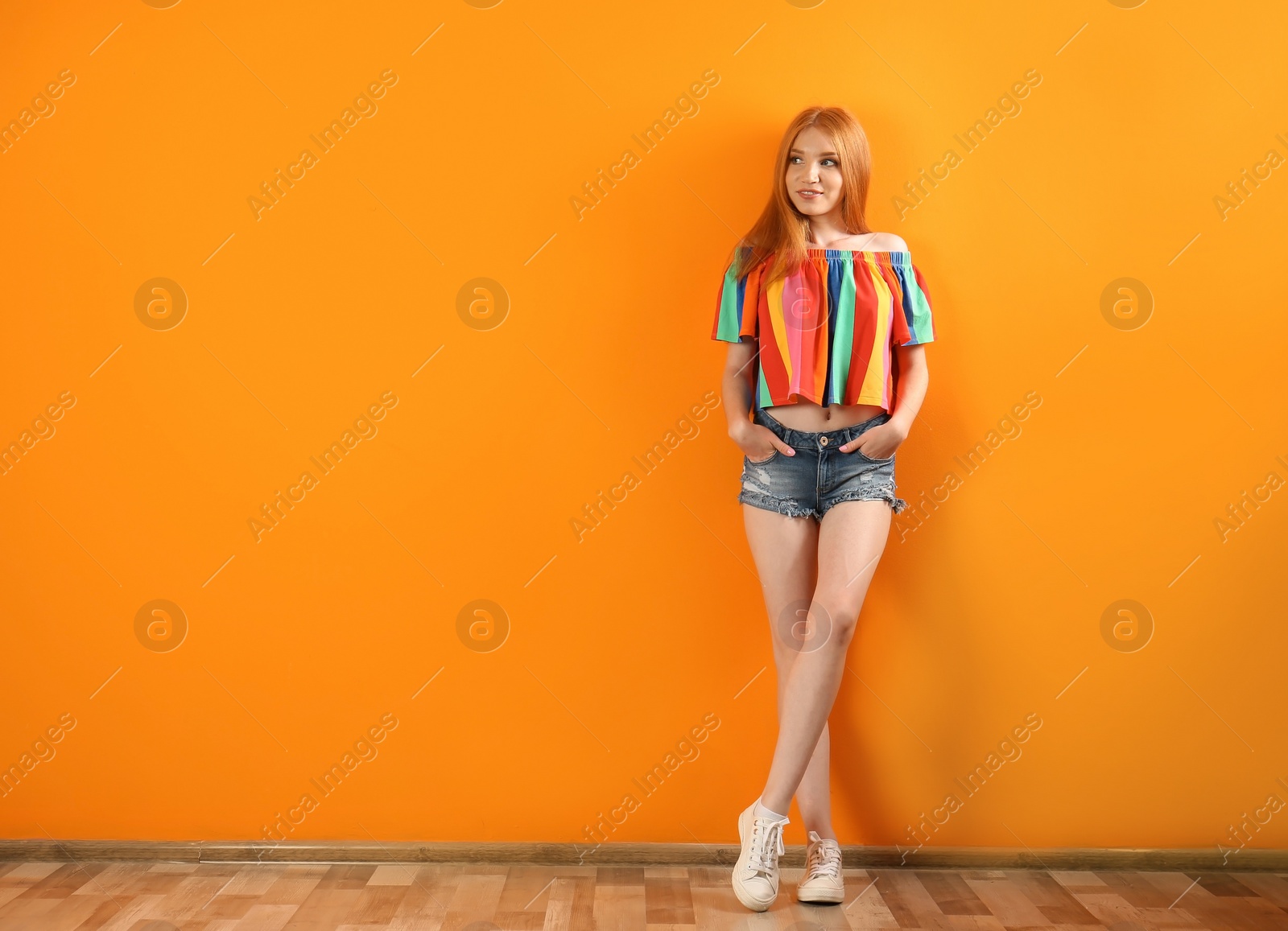 Photo of Young woman in stylish jean shorts near color wall