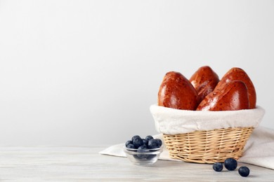 Photo of Delicious baked pirozhki and blueberries on wooden table, space for text