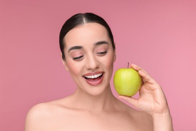 Beautiful young woman with apple on pink background
