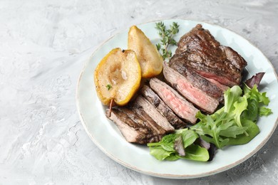 Photo of Pieces of delicious roasted beef meat, caramelized pear and greens on light textured table. Space for text