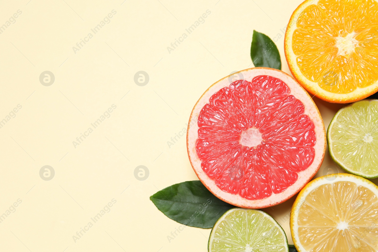 Photo of Different cut citrus fruits and leaves on beige table, flat lay. Space for text