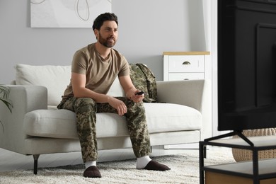 Photo of Soldier watching TV on sofa in living room. Military service