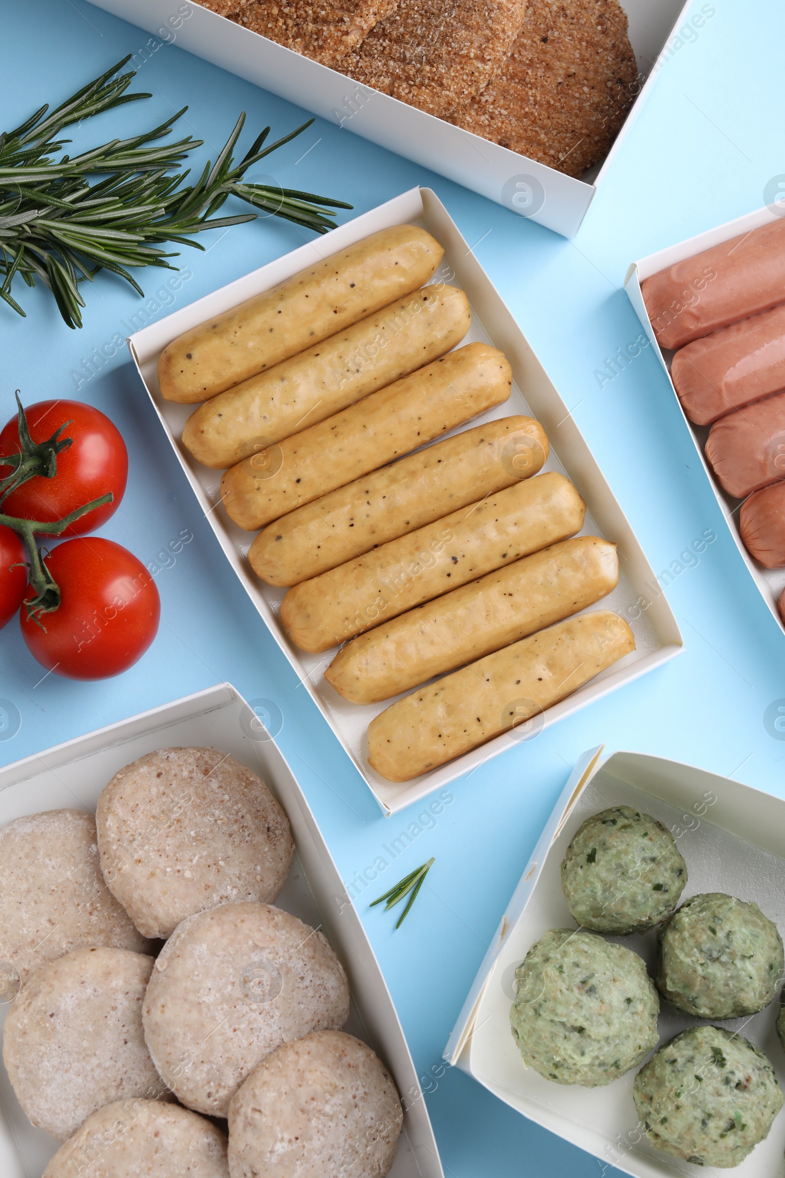 Photo of Many different raw vegan meat products, tomatoes and rosemary on light blue background, flat lay