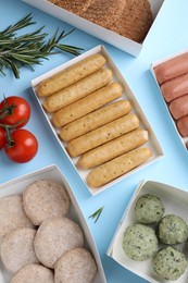 Many different raw vegan meat products, tomatoes and rosemary on light blue background, flat lay