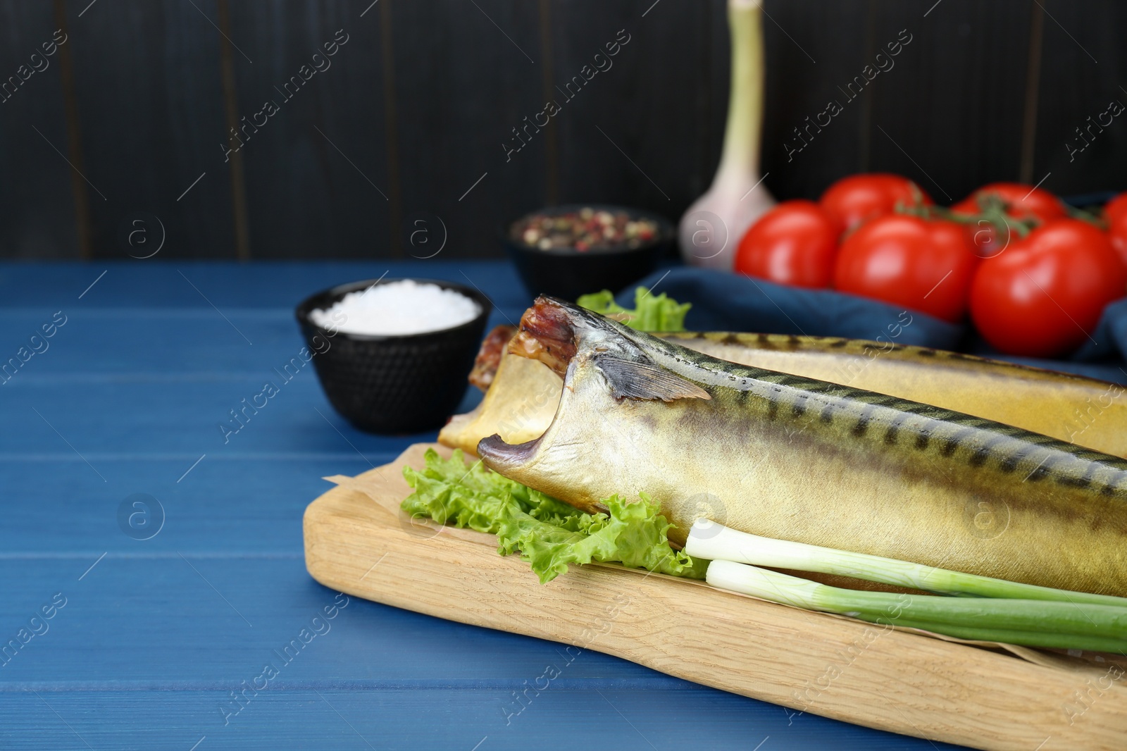 Photo of Delicious smoked mackerels, green onions and lettuce on blue wooden table, closeup. Space for text
