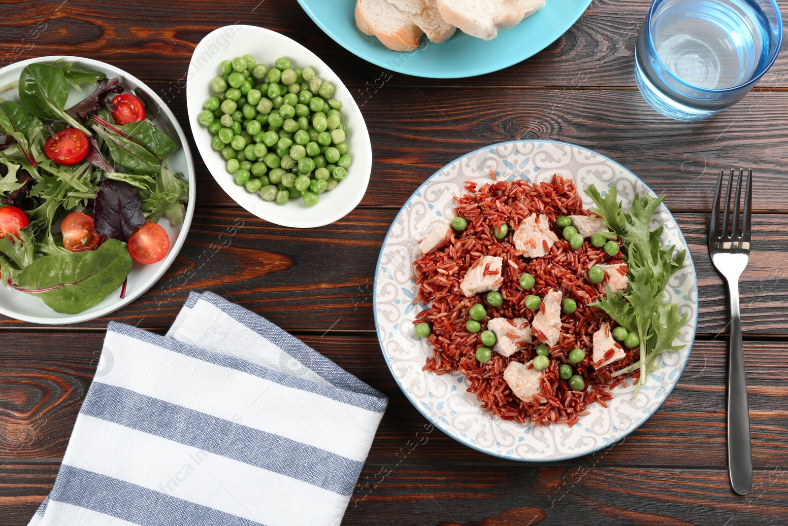 Photo of Tasty brown rice with meat and vegetables served on wooden table, flat lay