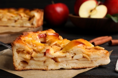 Photo of Slice of traditional apple pie on black wooden table, closeup