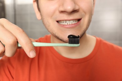 Man holding toothbrush with charcoal toothpaste on gray background, closeup