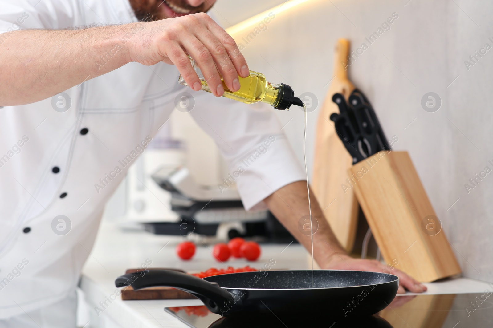 Photo of Chef pouring oil from bottle into frying pan indoors, closeup