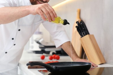 Chef pouring oil from bottle into frying pan indoors, closeup