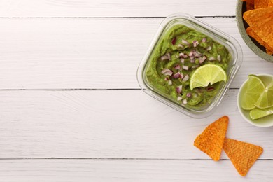 Photo of Bowl of delicious guacamole with onion, lime and nachos chips on white wooden table, flat lay. Space for text