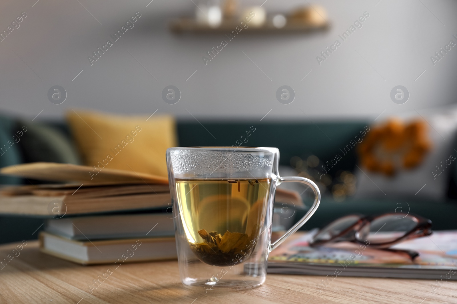 Photo of Glass cup of freshly brewed tea on wooden table in living room. Cozy home atmosphere