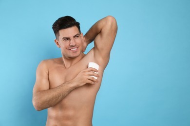 Photo of Handsome man applying deodorant to armpit on turquoise background, space for text