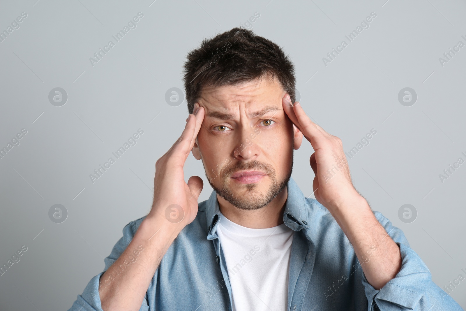 Photo of Man suffering from terrible migraine on light grey background