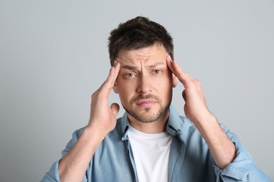 Man suffering from terrible migraine on light grey background