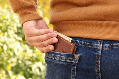 Photo of Man putting wallet with money in pocket of jeans outdoors, closeup