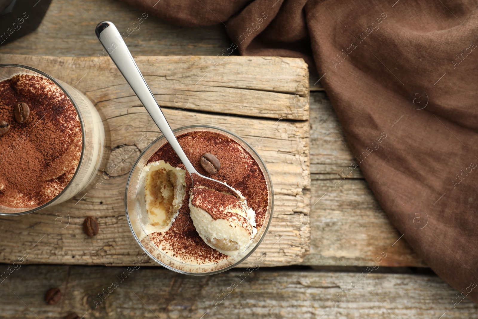 Photo of Delicious tiramisu in glasses, spoon and coffee beans on wooden table, top view