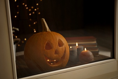 Photo of Composition with pumpkin head on windowsill, view through glass. Jack lantern - traditional Halloween decor